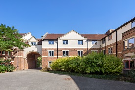 Exterior of a large three-storey red brick building, with trees and bushes in front of it.