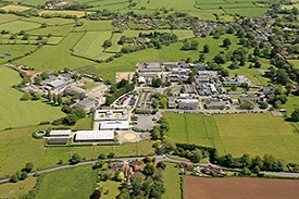 Aerial view of a rural landscape with lots of fields. There is a large cluster of buildings in the foreground, with some smaller clusters of houses further back.